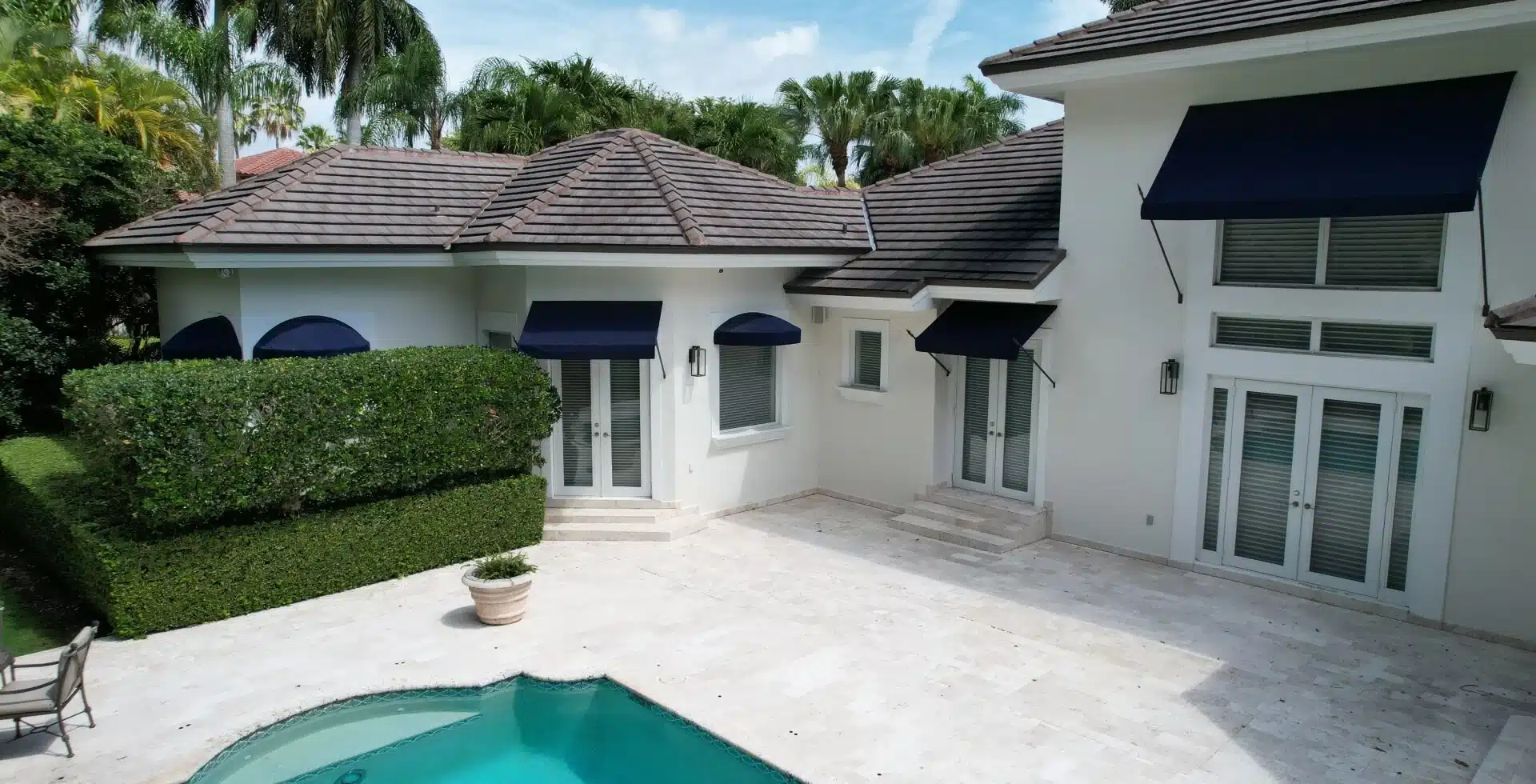 White home with navy awnings over impact windows by the pool
